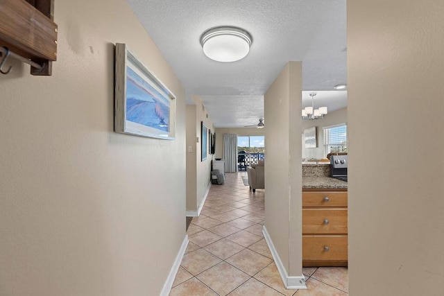 hall with a textured ceiling, a chandelier, and light tile patterned floors