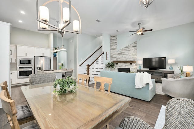 dining space with a fireplace, a high ceiling, dark hardwood / wood-style flooring, and ceiling fan with notable chandelier