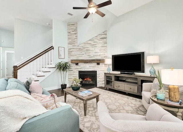 living room with ceiling fan, wood-type flooring, a tile fireplace, and a towering ceiling