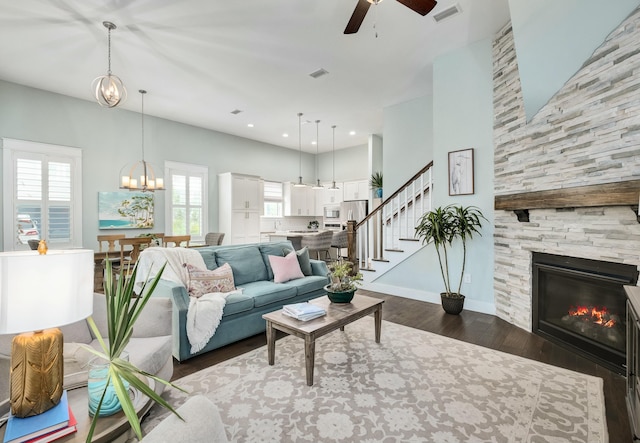 living room featuring ceiling fan with notable chandelier, dark wood-type flooring, and a tiled fireplace