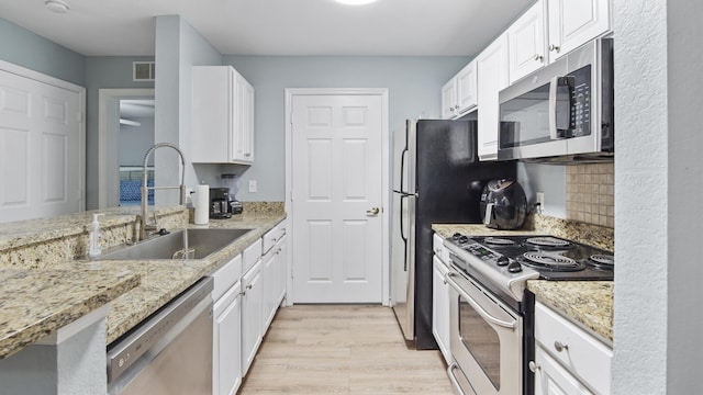 kitchen with light stone countertops, white cabinetry, sink, stainless steel appliances, and light hardwood / wood-style floors