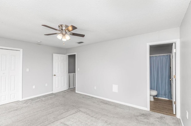 unfurnished bedroom with ensuite bath, ceiling fan, a textured ceiling, light colored carpet, and a closet