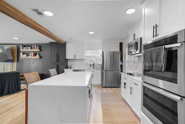 kitchen featuring light wood-type flooring, stainless steel appliances, a kitchen island, sink, and white cabinetry