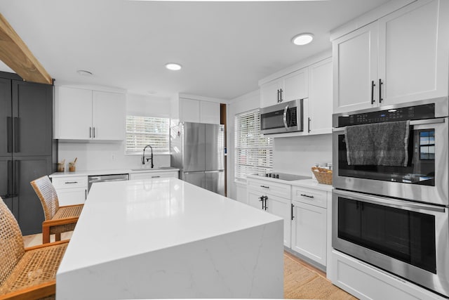 kitchen with sink, light hardwood / wood-style flooring, a kitchen island, white cabinetry, and stainless steel appliances