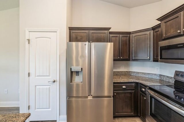 kitchen with appliances with stainless steel finishes, dark brown cabinetry, and dark stone counters