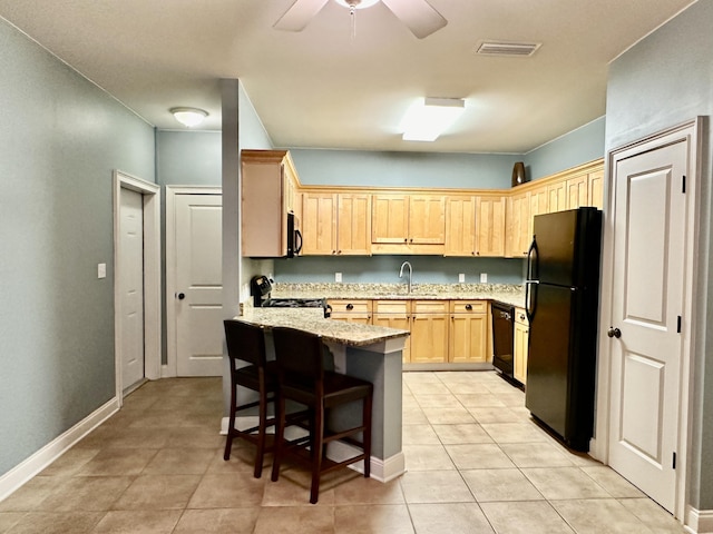 kitchen featuring light stone countertops, light brown cabinets, sink, a breakfast bar, and black appliances