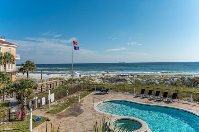 view of swimming pool featuring a beach view, a water view, and a hot tub