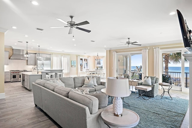 living room with ceiling fan with notable chandelier, crown molding, and light wood-type flooring