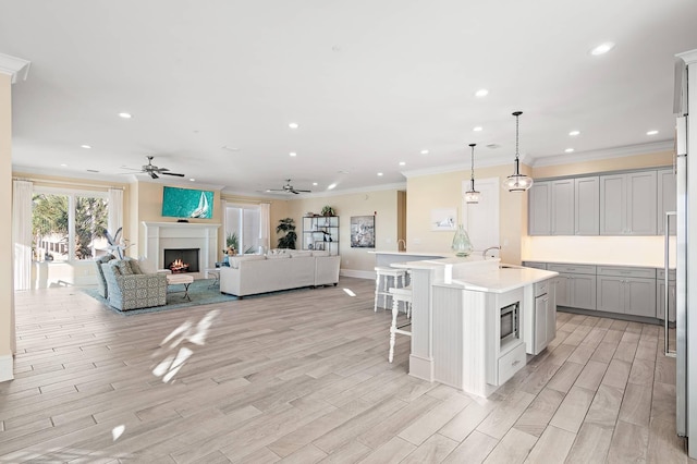 kitchen featuring pendant lighting, a kitchen island with sink, ceiling fan, stainless steel microwave, and a breakfast bar area