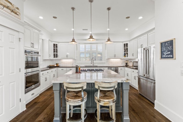 kitchen featuring appliances with stainless steel finishes, dark hardwood / wood-style flooring, a kitchen island, white cabinetry, and hanging light fixtures