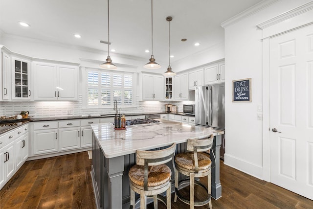 kitchen with hanging light fixtures, dark hardwood / wood-style floors, dark stone countertops, a kitchen island, and appliances with stainless steel finishes