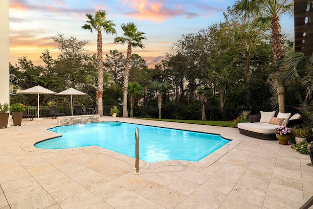 pool at dusk featuring pool water feature and a patio