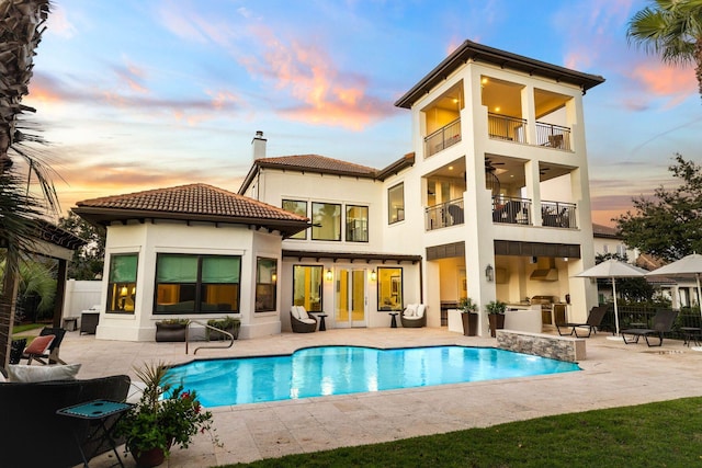 back house at dusk with a fenced in pool, a balcony, a patio, and an outdoor kitchen