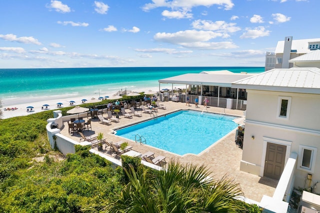 view of pool featuring a water view, a patio, and a beach view