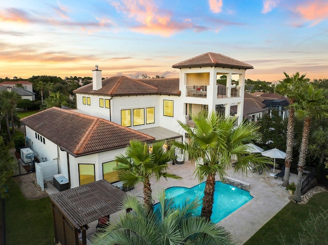 back house at dusk featuring a balcony and a patio area