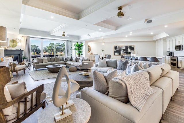 living room with beamed ceiling, ceiling fan, crown molding, and light hardwood / wood-style flooring