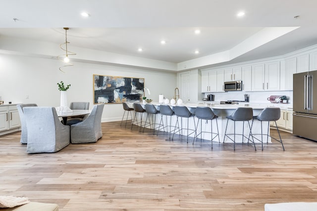 kitchen featuring hanging light fixtures, stainless steel appliances, a kitchen island with sink, and light hardwood / wood-style floors