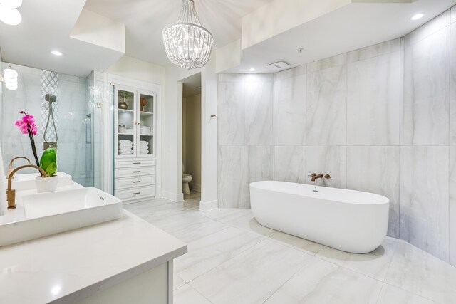 full bathroom with vanity, an inviting chandelier, tile walls, shower with separate bathtub, and toilet