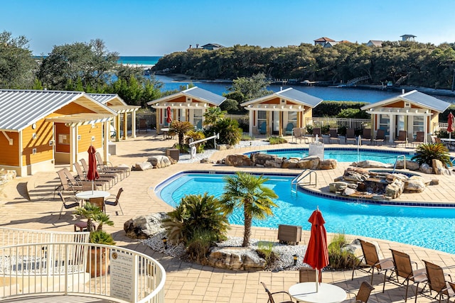 view of pool featuring a patio area, a water view, and an outdoor structure