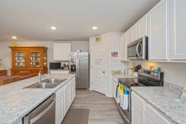 kitchen featuring white cabinets, sink, light wood-type flooring, light stone counters, and stainless steel appliances