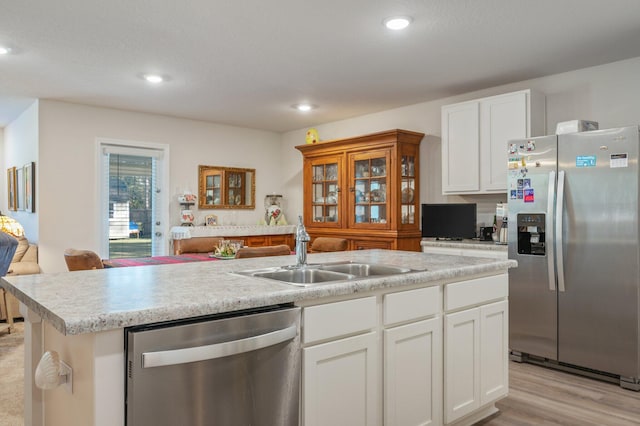 kitchen with white cabinets, a center island with sink, sink, light wood-type flooring, and stainless steel appliances