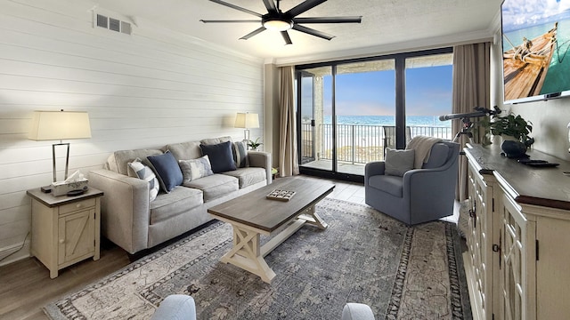 living room with floor to ceiling windows, ceiling fan, light hardwood / wood-style flooring, and wooden walls