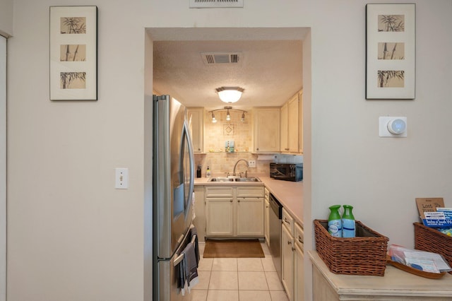 kitchen with tasteful backsplash, a textured ceiling, stainless steel appliances, sink, and light tile patterned floors