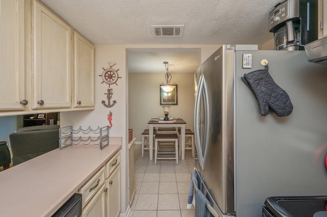 kitchen featuring a textured ceiling, stainless steel refrigerator, light tile patterned flooring, and decorative light fixtures