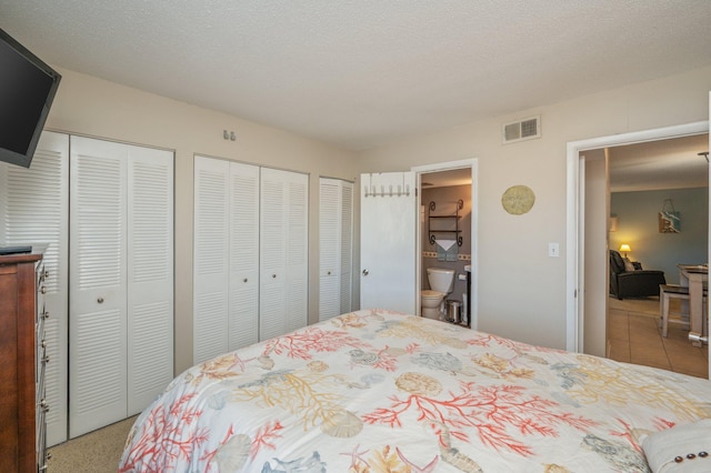 carpeted bedroom featuring ensuite bathroom, a textured ceiling, and multiple closets