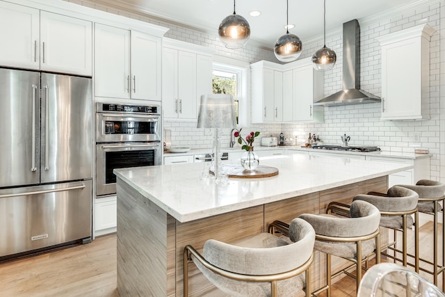 kitchen featuring white cabinets, a kitchen breakfast bar, wall chimney range hood, an island with sink, and stainless steel appliances