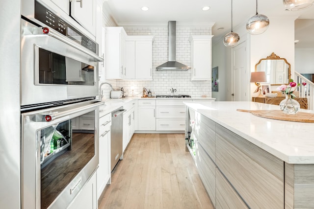 kitchen featuring crown molding, wall chimney exhaust hood, light wood-type flooring, white cabinetry, and stainless steel appliances