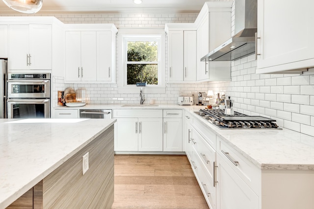 kitchen with appliances with stainless steel finishes, white cabinetry, light stone counters, and wall chimney range hood