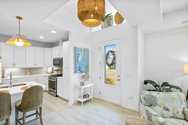 kitchen featuring pendant lighting, white cabinets, sink, appliances with stainless steel finishes, and light hardwood / wood-style floors