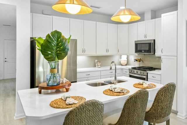 kitchen with sink, tasteful backsplash, a center island with sink, white cabinets, and appliances with stainless steel finishes