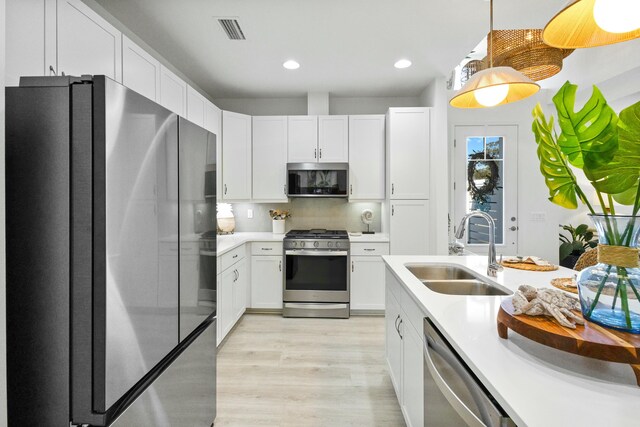 kitchen with sink, light hardwood / wood-style flooring, backsplash, white cabinets, and appliances with stainless steel finishes