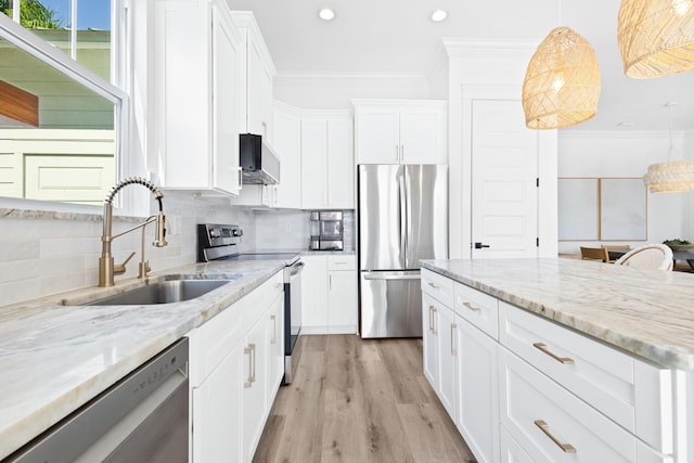 kitchen with backsplash, ornamental molding, stainless steel appliances, white cabinetry, and a sink