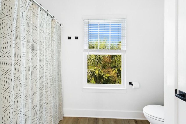 full bathroom featuring toilet, wood finished floors, baseboards, and a wealth of natural light