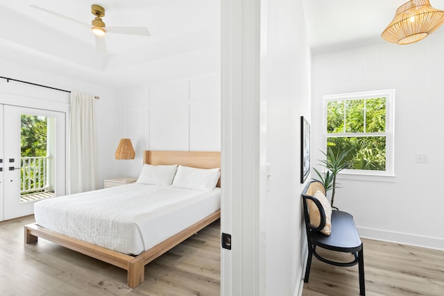 bedroom featuring access to exterior, light wood-style flooring, multiple windows, and a raised ceiling