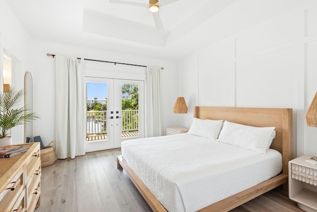 bedroom featuring light wood-type flooring, french doors, a raised ceiling, a ceiling fan, and access to outside