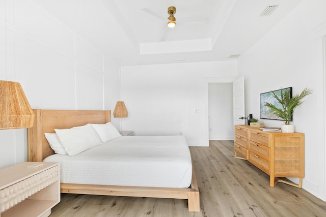 bedroom with a raised ceiling, baseboards, visible vents, and light wood finished floors