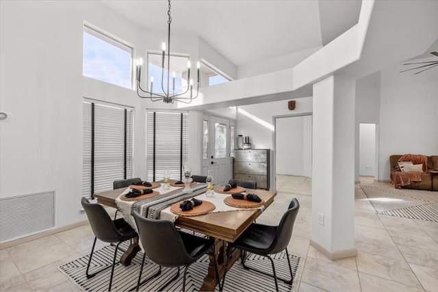 tiled dining area featuring ceiling fan with notable chandelier and a high ceiling