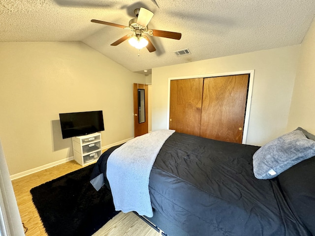 bedroom with vaulted ceiling, ceiling fan, a textured ceiling, light hardwood / wood-style floors, and a closet