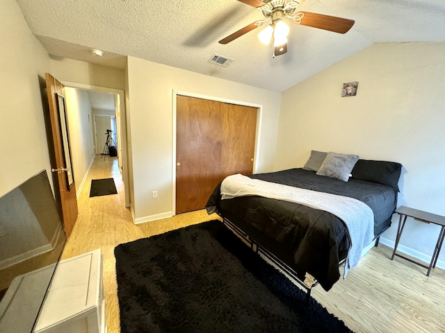 bedroom with lofted ceiling, light hardwood / wood-style flooring, ceiling fan, a textured ceiling, and a closet