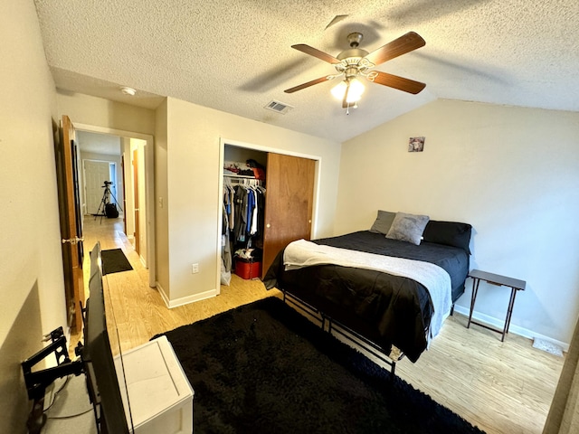 bedroom with ceiling fan, light hardwood / wood-style flooring, a textured ceiling, vaulted ceiling, and a closet