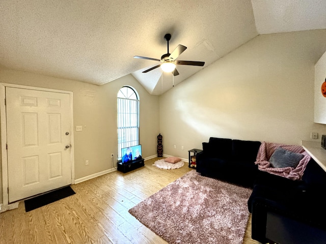 living room with a textured ceiling, ceiling fan, light hardwood / wood-style flooring, and vaulted ceiling