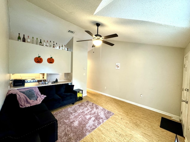 living room with a textured ceiling, light hardwood / wood-style floors, ceiling fan, and lofted ceiling