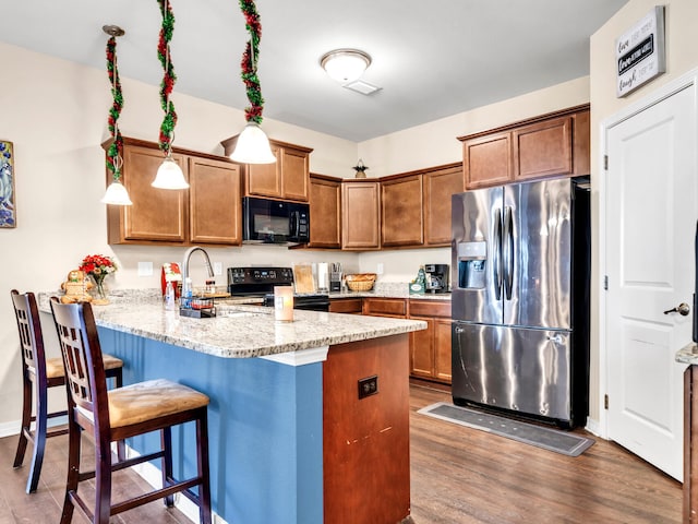 kitchen with dark wood-type flooring, black appliances, light stone counters, a kitchen bar, and kitchen peninsula