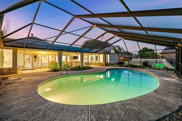 pool at dusk featuring glass enclosure and a patio area