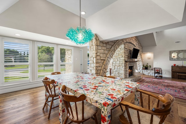 dining space with a fireplace, wood-type flooring, and high vaulted ceiling