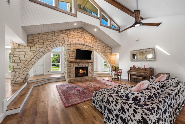 living room featuring ceiling fan, a fireplace, beam ceiling, hardwood / wood-style flooring, and high vaulted ceiling